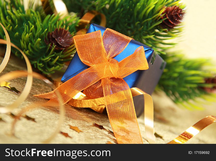 Christmas blue gift box with orange bow against fir branch on golden background. Christmas blue gift box with orange bow against fir branch on golden background