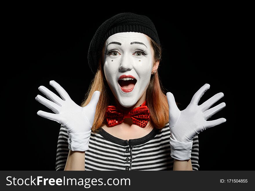 Happy female mime on black background. Cute actress is using exaggerated face expressions, hand gestures and no words in acting a pantomime.