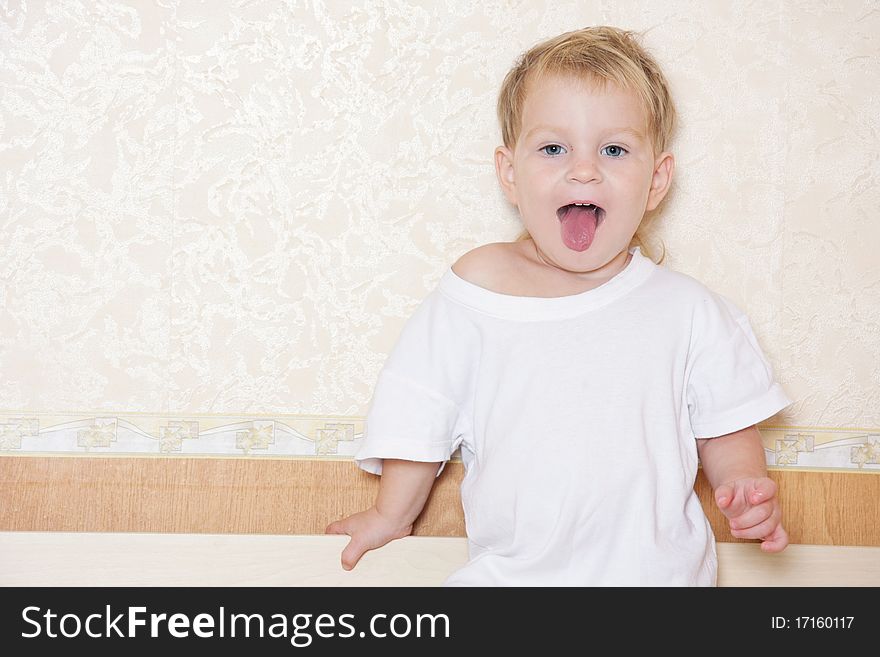 Cute child showing his tongue on room background