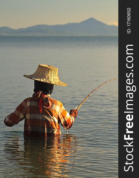 Thai woman fishing in the sea at sunset wearing traditional clothing and hat