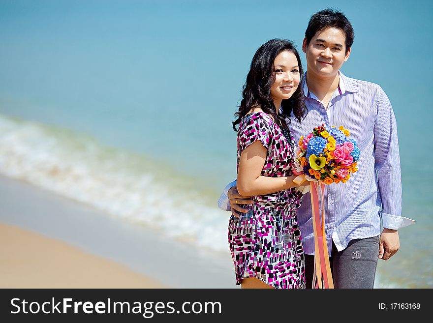 Attractive couple standing together on the beach with beautiful bouquet