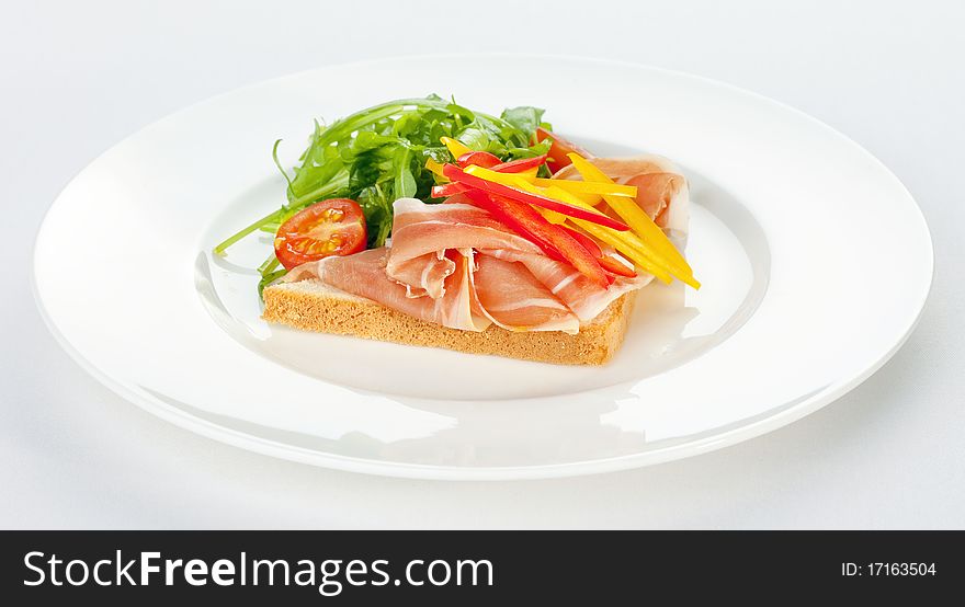 Sandwich with ham, tomatoes, paprika and ruccola on a white plate