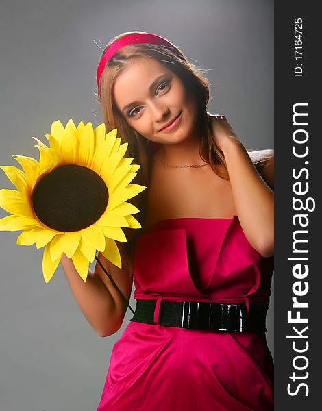 Girl with a sunflower in a pink dress on a grey background