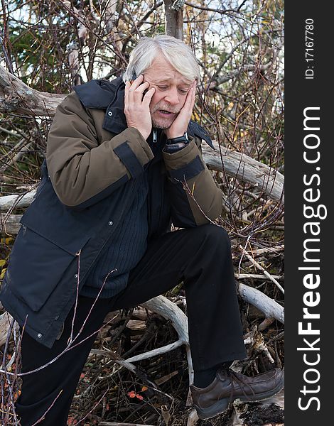 Mature busy man with grey hair in forest talking on the phone in autumn day. Mature busy man with grey hair in forest talking on the phone in autumn day.