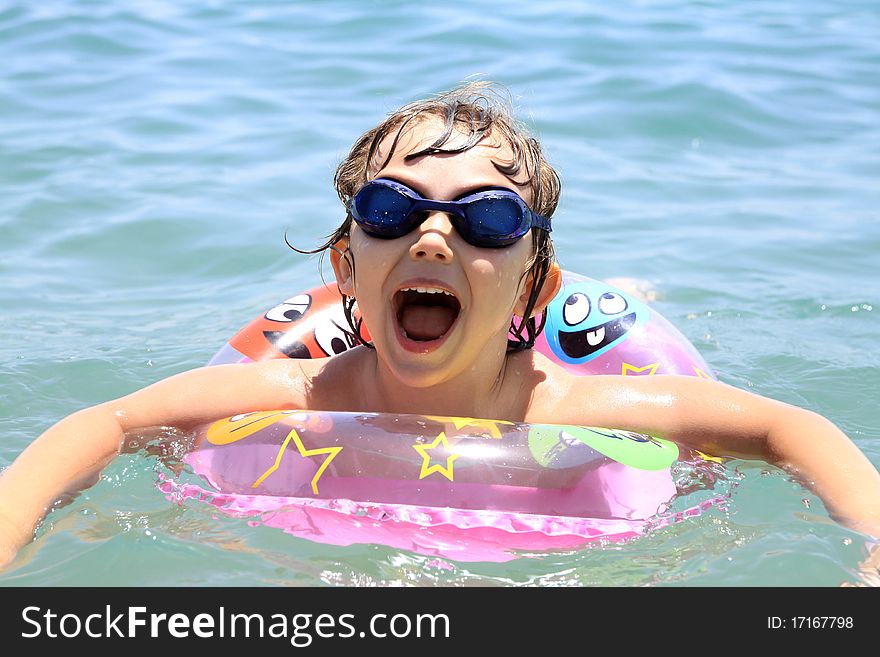 A small child swims in the sea. The girl in the pink circle swims and swimming glasses. Summer