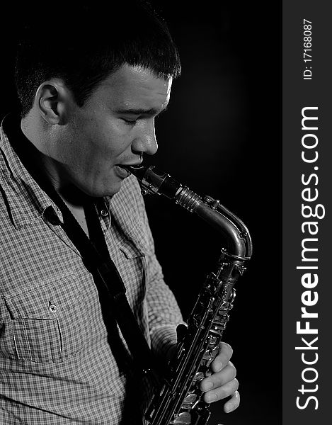 Young handsome man playing music on saxophone. black background