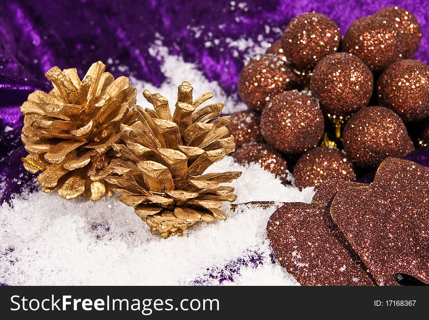 Christmas gold cones with brown balls on the snow and on violet background. Christmas gold cones with brown balls on the snow and on violet background.