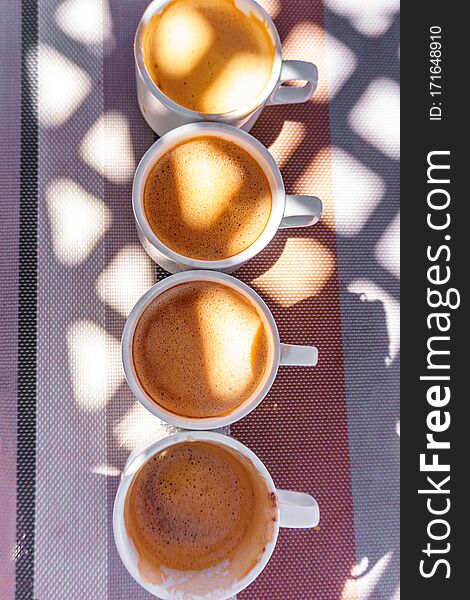 Four cups of coffee on the table illuminated by the sun through the lattice roof top view. Four cups of coffee on the table illuminated by the sun through the lattice roof top view