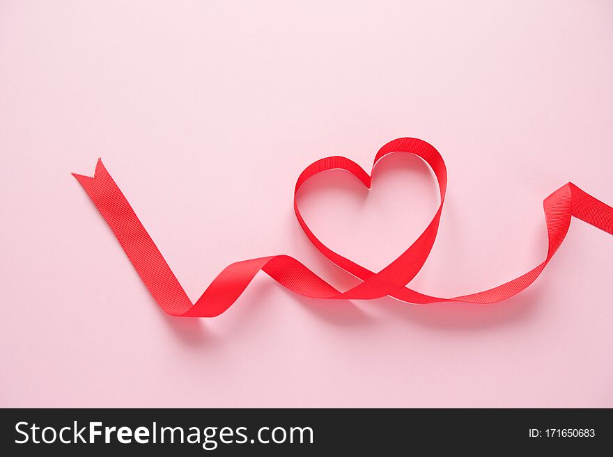 Red ribbon in the shape of a heart on a pink background