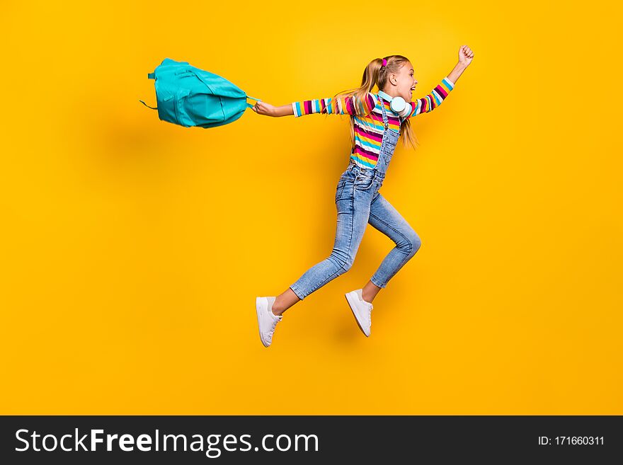 Yeah holidays begin. Full size profile side crazy schoolkid jump run hold blue backpack bag have headset wear striped sweater denim jeans isolated over bright shine, yellow color background