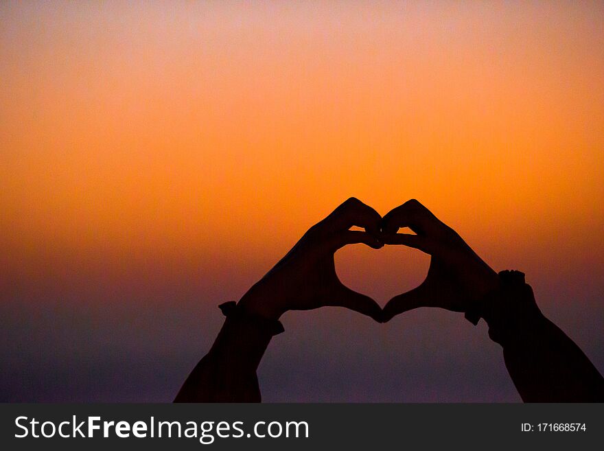 Silhouette of heart made by kids hand at sunset