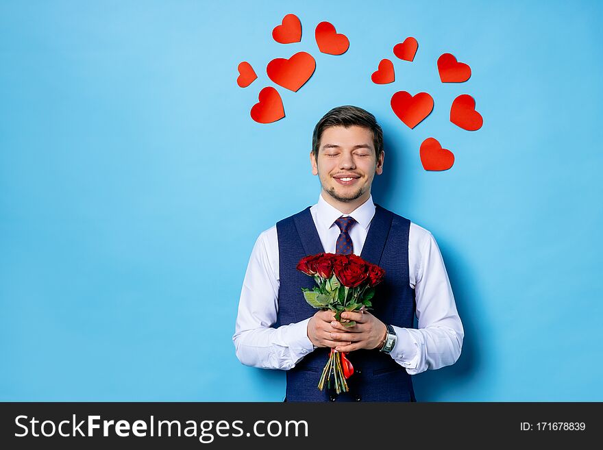 Guy in tuxedo isolated over blue background. smiling caucasian male in formal wear stand with closed eyes holding red roses in hands and dream, waiting for valentines day. love, celebration concept. Guy in tuxedo isolated over blue background. smiling caucasian male in formal wear stand with closed eyes holding red roses in hands and dream, waiting for valentines day. love, celebration concept