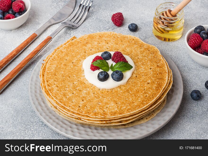 Plate of delicious thin pancakes with berries on grey table Copy space