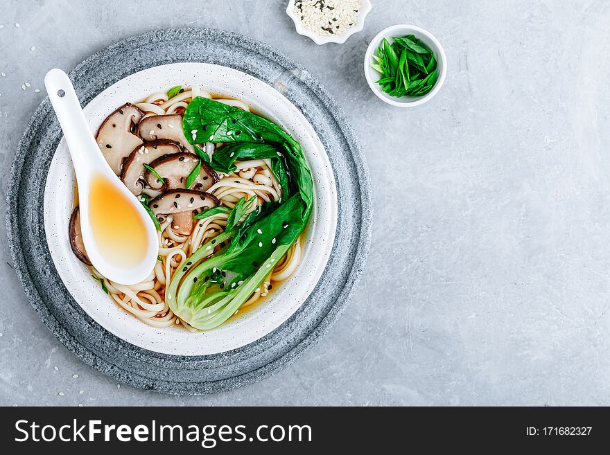 Asian Vegetarian Udon or Ramen noodles soup in bowl with Shiitake mushrooms and Bok Choy on grey stone background. Top view, copy space