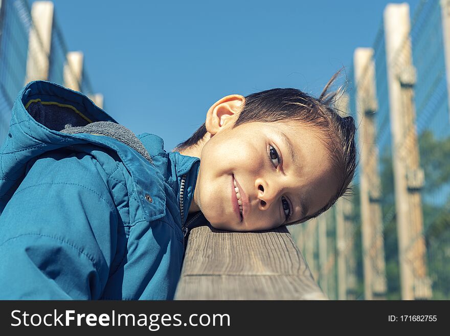 Happy little boy leaning his head on wooden railing. Cute kid.