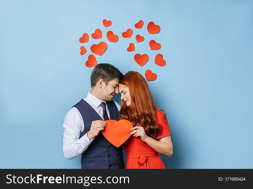 Portrait of cute caucasian couple holding heart made from cardboard, stand next to each other and feel tenderness. isolated blue background. love concept. Portrait of cute caucasian couple holding heart made from cardboard, stand next to each other and feel tenderness. isolated blue background. love concept