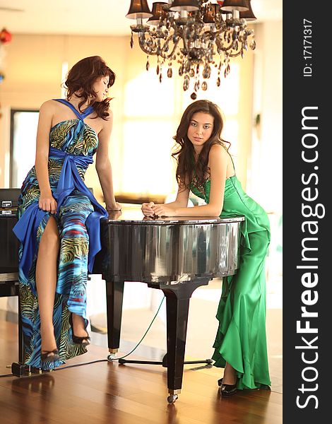 Two beautiful young women with long dresses standing at a piano, shallow depth of field. Two beautiful young women with long dresses standing at a piano, shallow depth of field