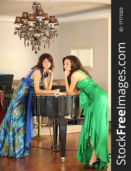Two beautiful young women with long dresses standing at a piano, shallow depth of field, focus on left girl. Two beautiful young women with long dresses standing at a piano, shallow depth of field, focus on left girl