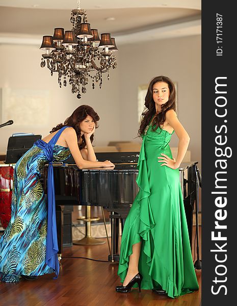 Two beautiful young women with long dresses standing at a piano, shallow depth of field. Two beautiful young women with long dresses standing at a piano, shallow depth of field