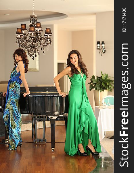 Two beautiful young women with long dresses standing at a piano, shallow depth of field, focus on front girl. Two beautiful young women with long dresses standing at a piano, shallow depth of field, focus on front girl