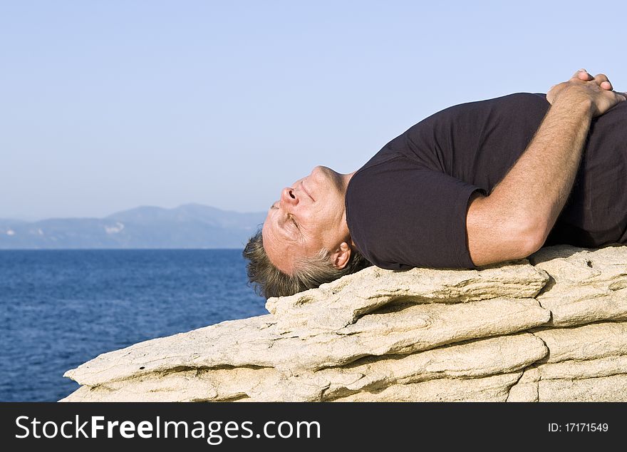 Color landscape photo of a mature man laying on a rock and sunbathing on the island of Paxos in the Ionian region of Greece. Color landscape photo of a mature man laying on a rock and sunbathing on the island of Paxos in the Ionian region of Greece.