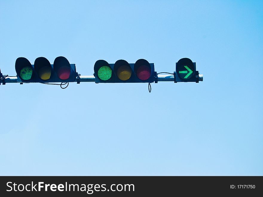 Green color on the traffic light on the blue sky background