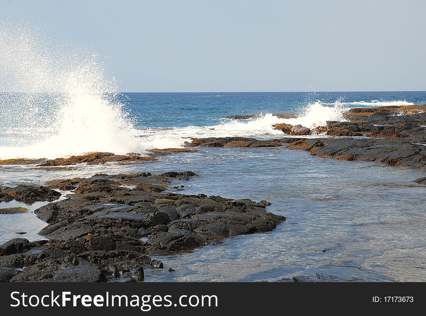 The Pacific Ocean meets a black lava tidal pool in the Hawaiian Islands. The Pacific Ocean meets a black lava tidal pool in the Hawaiian Islands