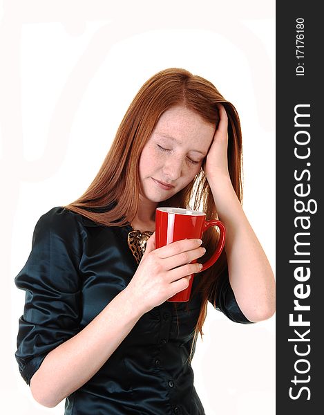 A young woman with long red hair with a headache holding her head
and a mug of coffee, in a green blouse for white background. A young woman with long red hair with a headache holding her head
and a mug of coffee, in a green blouse for white background.