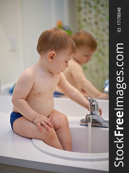 Toddler learning to turn the water on and off. Sitting on a bathroom counter with his feet in the sink in front of a mirror. Toddler learning to turn the water on and off. Sitting on a bathroom counter with his feet in the sink in front of a mirror.