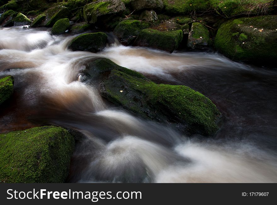 Motion blurred wild river flowing over the mossy stones