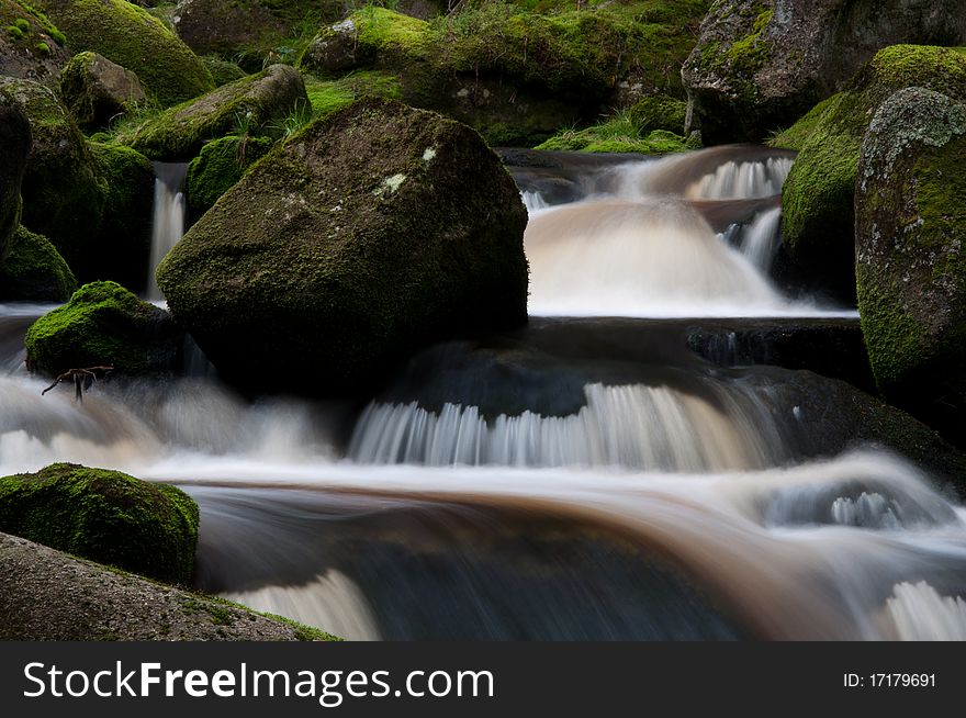 Motion blurred wild river flowing over the mossy stones