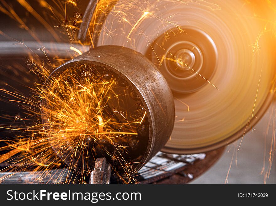 Close-up on the sides fly bright sparks from the angle grinder machine. A young male welder welding a metal product with angle grinder in the garage. Close-up on the sides fly bright sparks from the angle grinder machine. A young male welder welding a metal product with angle grinder in the garage