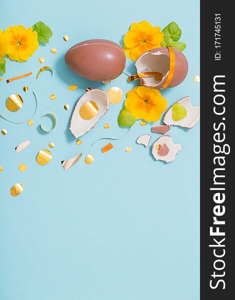 Easter chocolate egg with golden confetti and spring flowers on blue background