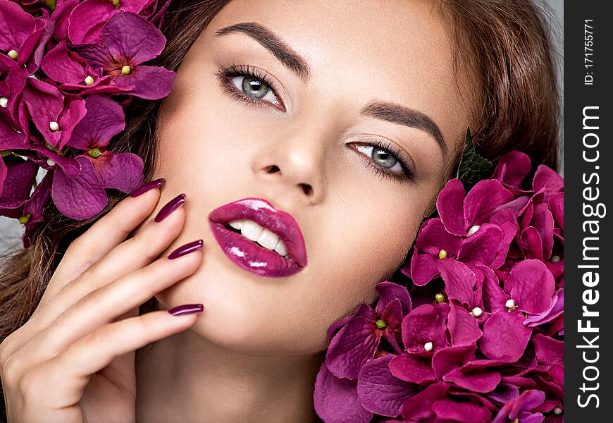 Beautiful  woman with purple make-up of lips and fingernails. Closeup woman`s portrait with flowers. Young caucasian gorgeous attractive girl. Model. Vivid make-up. Sexy female. Violet fingernails