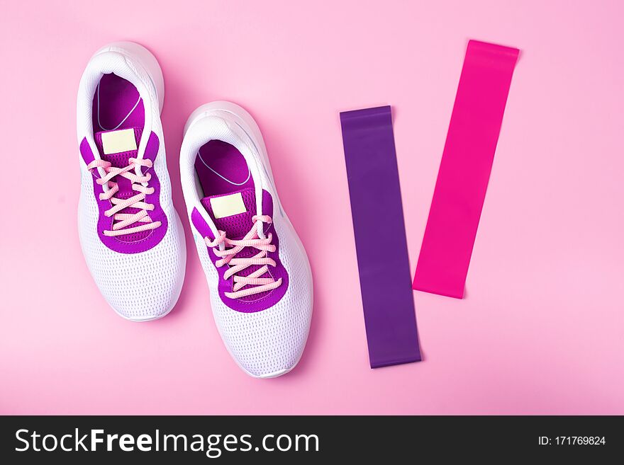 Women`s white sneakers on a pink background. The view from the top