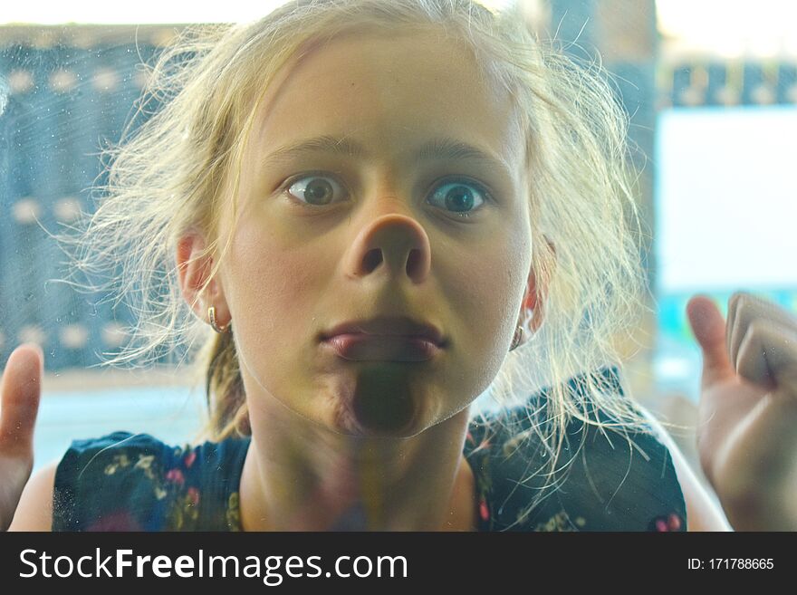 Funny portrait of a girl. The child stuck to the glass. Girl looking out the window. Flattened nose. Perky teen. Funny portrait of a girl. The child stuck to the glass. Girl looking out the window. Flattened nose. Perky teen