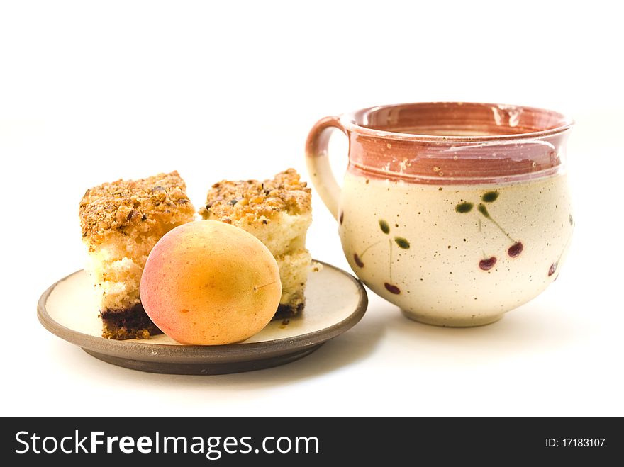 A cup of milk and a plate on which lay pieces of cake and a ripe apricot, on a white background. A cup of milk and a plate on which lay pieces of cake and a ripe apricot, on a white background