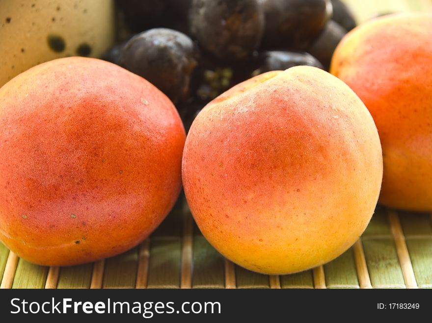 Yellow ripe apricots lie on the background of the cup and grapes on a green mat, close-up