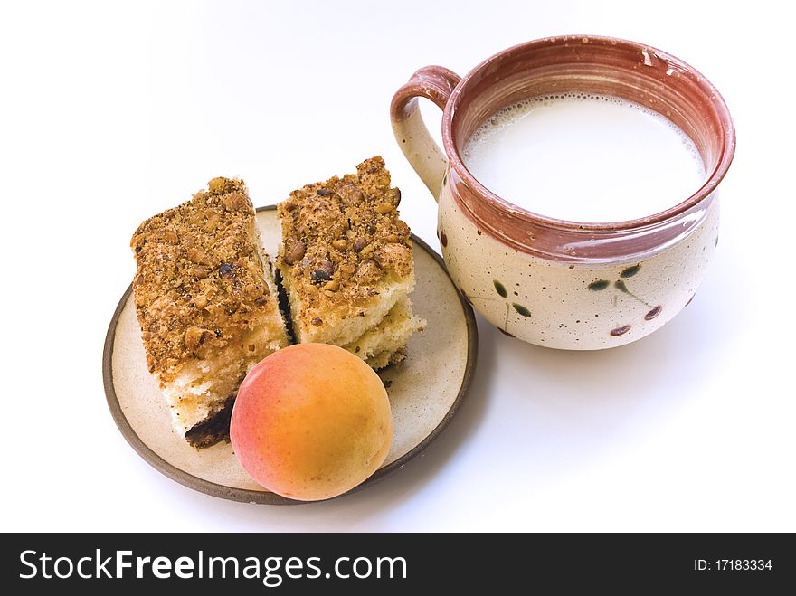A cup of milk and a plate on which lay two pieces of cake and a ripe apricot, on a white background. A cup of milk and a plate on which lay two pieces of cake and a ripe apricot, on a white background
