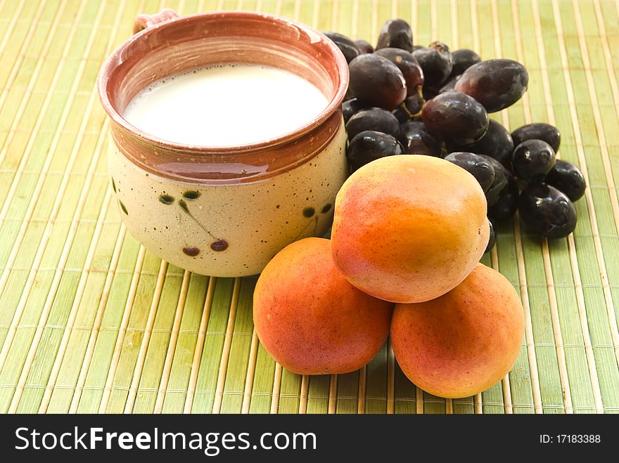 A cup of milk, three ripe apricots and brush the blue grapes on a green mat. close-up. A cup of milk, three ripe apricots and brush the blue grapes on a green mat. close-up