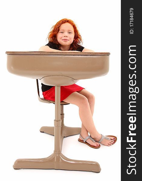 Adorable 7 year old red hair girl sitting in school desk over white background smiling. Adorable 7 year old red hair girl sitting in school desk over white background smiling.