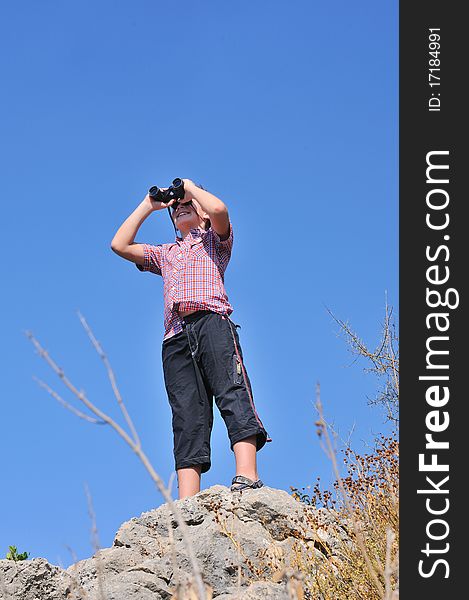 Boy stands atop a mountain and sees the neighborhood through binoculars. Boy stands atop a mountain and sees the neighborhood through binoculars