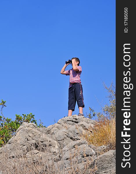 Boy stands atop a mountain and sees the neighborhood through binoculars. Boy stands atop a mountain and sees the neighborhood through binoculars