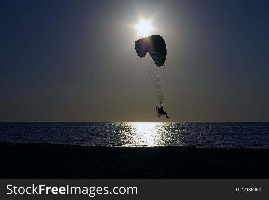 A person flying a parasail in front of the setting sun off of the beach in St. Petersburg Florida