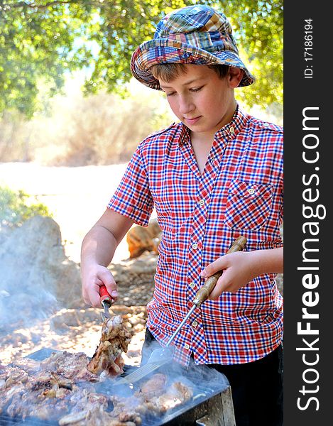 Teenager in a park on a holiday to cook meat and steaks on the grill. Teenager in a park on a holiday to cook meat and steaks on the grill