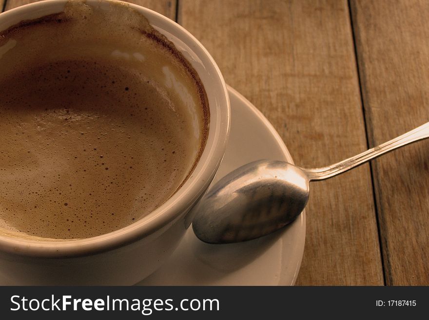 Having a cup of coffee concept; closeup image of a coffee in a white cup and saucer, with a teaspoon, isolated on a wooden table