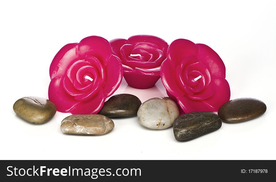 Red rose shaped candles sit against a white background with spa rocks. Red rose shaped candles sit against a white background with spa rocks