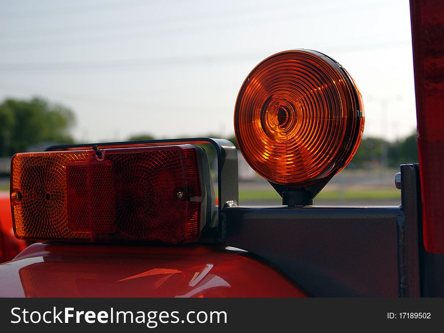 A close up of Tail Lights and Caution Light turn signal from a tractor with greenery in partial view with sky in background. A close up of Tail Lights and Caution Light turn signal from a tractor with greenery in partial view with sky in background