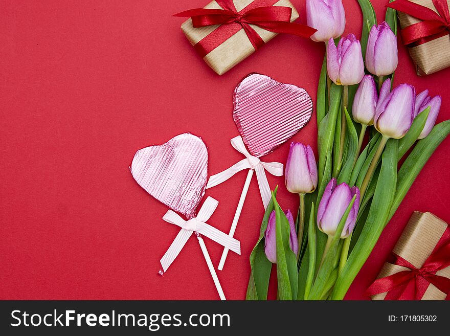 Pink Or Purple Tulip Flowers, Heart Shaped Chocolate And Gift Boxes On Red Background. Top View With Copy Space