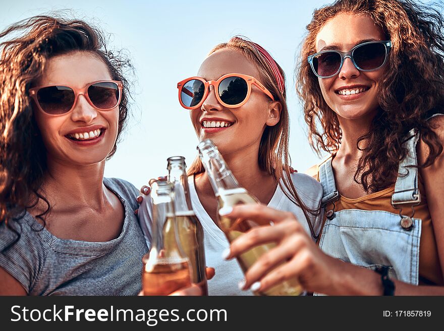 Three young women standing and clinking beer together